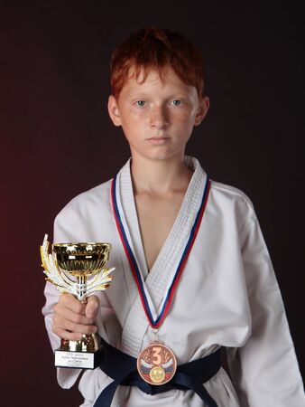 Bronze medalist of with a medal on his chest keeps a cup while wearing gloves の写真素材