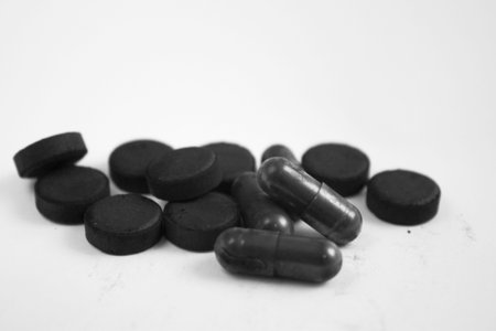 Charcoal black capsule tablets and pills in a heap on a white backgroundの写真素材