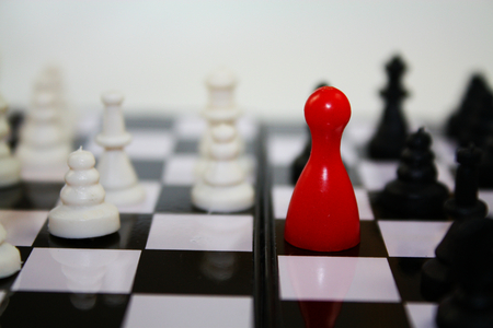 Chess game with bright red figurine for ludo on chessboard with other chess pieces.の写真素材