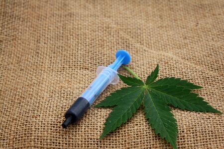Hash oil phoenix tears medicine in little syringe with a cannabis marijuana leaf on linen jute surfaceの写真素材
