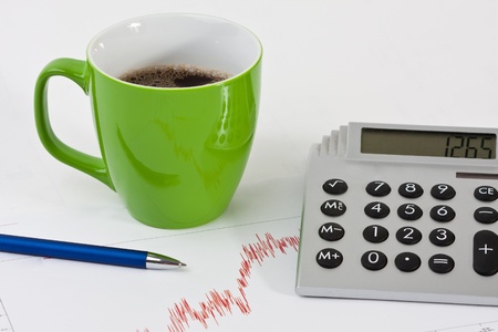 Close-up of a desk with a coffee cup, pen, a calculator and a balance sheet bendの写真素材