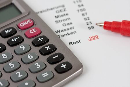 Closeup of a calculator and a red pen along with a negative budget planningの写真素材