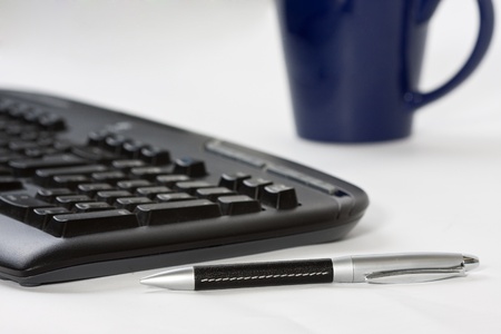 Close-up of a desk with computer keyboard, pen and coffee cupの写真素材