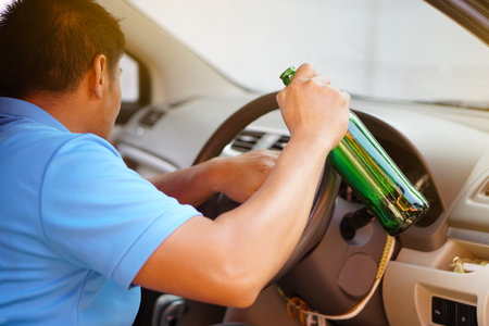 Asian drunk man holds bottle of beer to drink in car. Concept : Stop driving while drinking alcohol or whiskey campaign. Illegal and dangerous to drive vehicle that leads to accideの写真素材