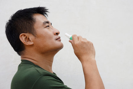 Asian man uses inhaler to smell  for relieve dizzy and faint symptoms. Concept : health problem, sickness and remedy. Increases freshness, reduces dizziness and stuffy nose.の写真素材