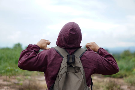 Back View of man wears brown hoodie cloth and backpack, stand outdoor, enjoy nature sightseeing....