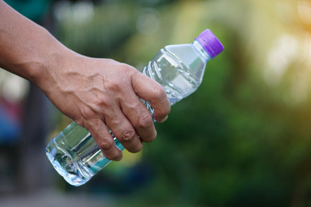 Closeup hand holds drinking water bottle with purple cap.   Concept : Drinking water for health, Healthy lifestyle. Quenching thirst, reduce fatigue, refresh body.の写真素材