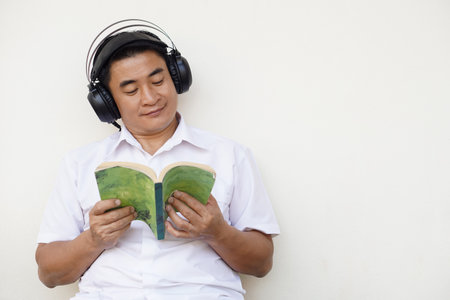 Asian man reads book and wears headphone listen to soft music to make concentration in reading. Concept, free time, pastime, hobby, Relax with music.の写真素材