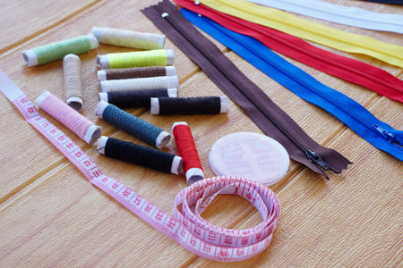 Sewing equipment, measuring tape, spools of thread and zips on brown wooden background. Concept,...