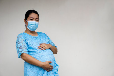 Pregnant Asian woman wears hygienic face mask, holds her big belly, 9 months pregnancy. Concept : Pregnancy  health care. Aged pregnant mother.の写真素材