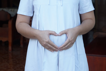 Closeup 6 month pragnant woman wears white dress, hands touch her big belly. Concept, pragnancy, motherhood. Health care. loveの写真素材