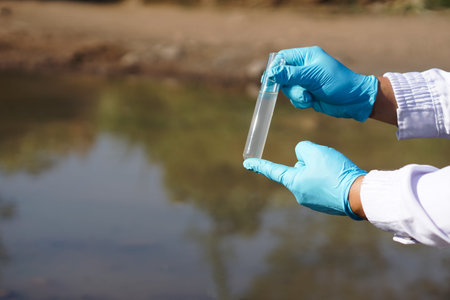 Closeup researcher hands wears blue gloves holds test glass tube that contain sample water from the...