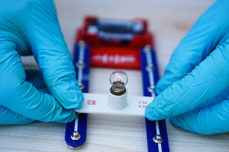Close up hands wear blue gloves holds mini light bulb kit to demonstrate science experiment about...