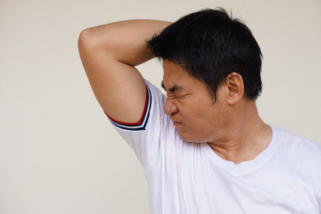 Asian man checks his body odor during he feels hot, raises right arm up, smells his armpit, underarm. Concept : health problem. Unpleasant body odor , smell nasty reaction. Negativの写真素材