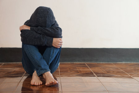 Depressed boy sits alone on the floor, feeling sad and cry, hug his knee. Concept : Emotional expression. Guilty, negative feeling. Introvert kid. Be bullied.の写真素材