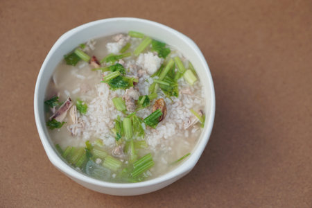 Homemade boiled rice, porridge or Thai traditional rice soup with minced pork, dried squid and vegetable on brown background. Concept, easy delicious food menu breakfast.の写真素材
