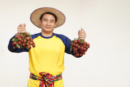Handsome Asian man farmer wears hat, yellow shirt, holds litchi fruits. Concept, agriculture...