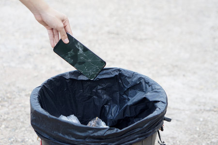 Closeup hand throw broken smartphone into the bin.Concept, hazardous  electronic waste should sort...