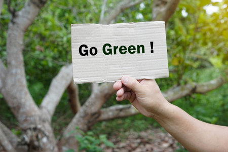 Hands hold paper sign with text  Go Green! in forest. Concept, campaign people around the world to stop activities that can cause global warming. Do eco friendly activity.の写真素材