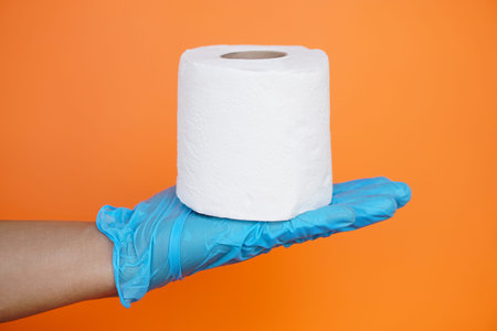 Close up hand holds roll of white tissue paper, isolated on orange background. Concept, cleaning...
