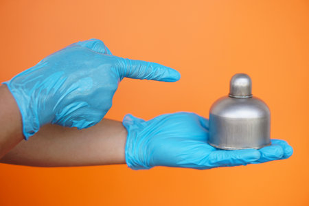 Close up  hands wears blue gloves point to alcohol burner  which used in laboratory , isolated on orange background. Concept, tool for doing science experiment.の写真素材