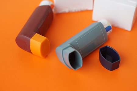 Asthma inhalers on orange background. Concept, Pharmaceutical products for treatment symptoms of asthma or COPD. Use under prescription. Health care device at home.の写真素材