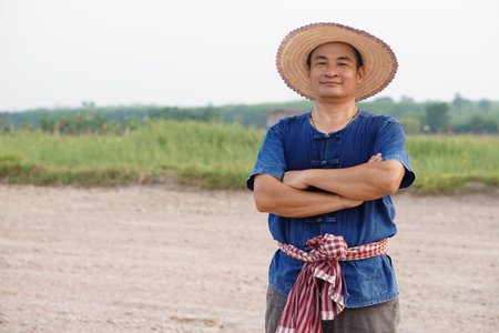 Handsome Asian man farmer wears hat, blue shirt, crossed arms on chest , feel confident.  Concept , Agriculture occupation. Thai Farmer .の写真素材