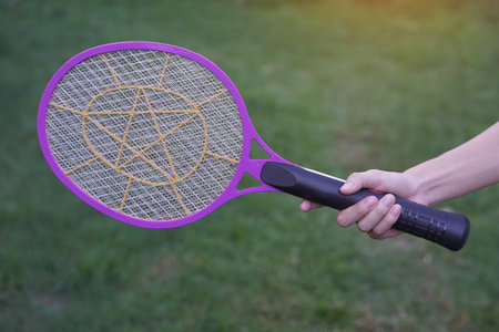 Closeup hand holds mosquito electric swatter racket. Concept, electric device to kill mosquitoes, insects, bugs by swatting to flying insects.の写真素材