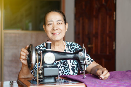 Happy senior Asian woman tailor is sewing cloth by vintage sewing machine at home. Concept, Senior ...