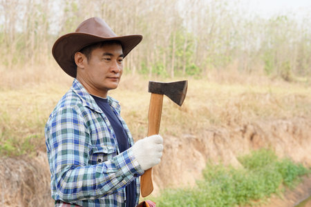 Asian gardener hold axe to cut trees in forest. Concept woodcutter deforestation. Working in garden. Hard working. Axe is Thai traditional tool for carpenter , lumberjack, handymanの写真素材