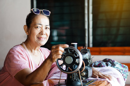 Happy senior Asian woman tailor is sewing cloth by vintage sewing machine at home. Concept, Senior ...