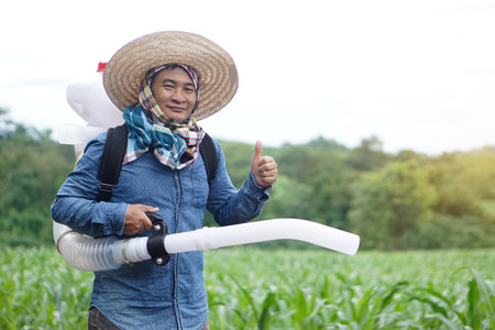 Asian man farmer carry fertilizer sprayer machine on back, stand at garden. Concept, farmer use engine facilitator tool in agriculture. Easy and fast for sowing.の写真素材