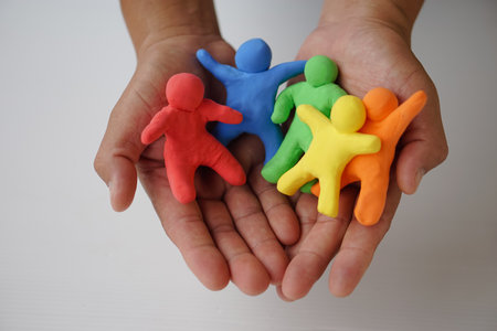 Close up hands holds colorful plasticine people. Human figures from plasticine sculpture.  Concept, friendships, partnerships and relationships between people.の写真素材