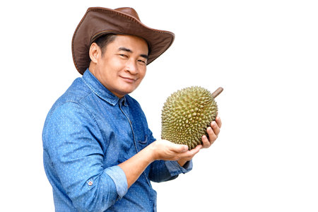 Handsome Asian man farmer wears hat, blue shirt, holds durian fruit,feels confident. Concept, agriculture occupation. Thai farmers grow durian fruits as economic and export cropの写真素材