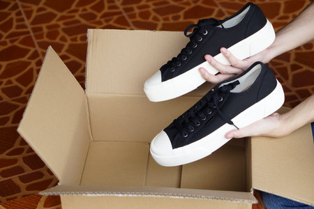Close up customer holds new shoes from cardboard box from shopping. Concept, footwears , Checking the condition of goods from shopping online or shoe shops. Stylish sneakers.の写真素材