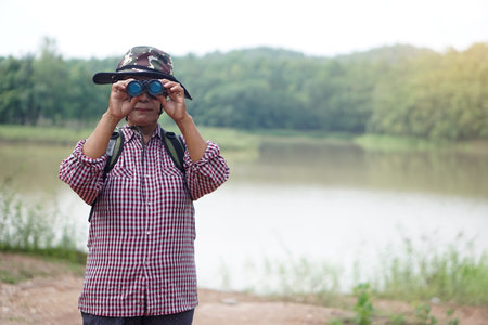 Asian senior woman goes traveling alone, use binocular to survey nature at the lake. Concept,...