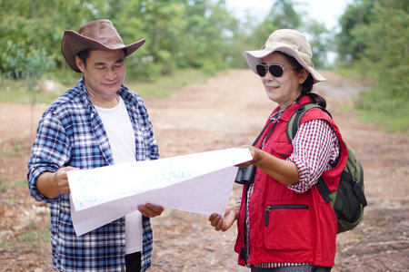 Asian man and woman travellers holds paper map to explore natural route for trekking. Concept,...