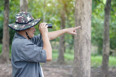 Asian man ecologist use binocular to survey nature in forest. Concept, nature exploration. Ecology...