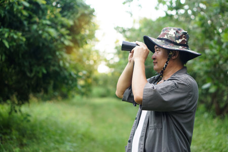 Asian man ecologist use binocular to survey nature in forest. Concept, nature exploration. Ecology study. Pastime activity, lifestyle. Explore environment. Traveling aloneの写真素材