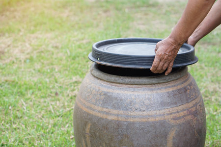 Closeup hands hold lid to cover water jar to protect from mosquitoes to breed inside or other  insects or dust go into water. Concept, campaign to stop mosquitoes cycle to lay eggsの写真素材