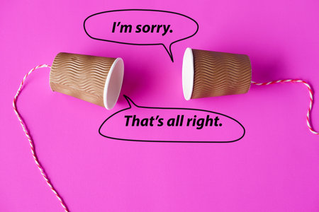 Paper cups with string on pink background. Bubble speech with words. Hello, I'm sorry. That's all right. Concept, English conversation. Teaching aid. Cummunication.の写真素材