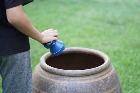 Close up boy hold flashlight to explore mosquito larvae or insects that breed inside water jar. Concept, campaign to stop mosquitoes cycle to lay eggs in water container.の写真素材