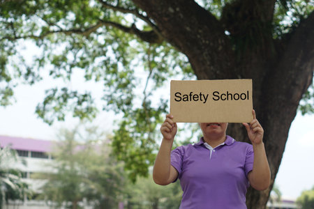 Woman hold paper placard  with text Safety School, stand under the tree. Concept, protest, campaign for schools must be the safe place for students in every situation.の写真素材