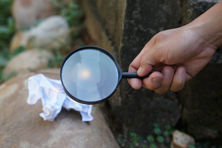 hand holding a magnifying glass with crumpled paper on stone backgroundの写真素材