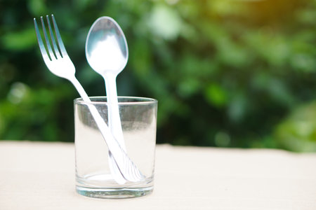 Empty glass with spoon and fork on wooden table with nature background.の写真素材