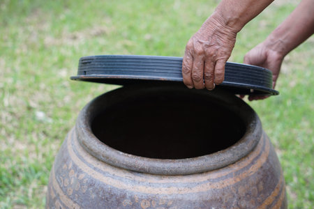 Hand of old woman pouring water into a big clay pot in the garden