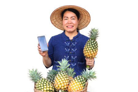 Asian fruit seller wear hat, blue shirt, holds pineapple fruit and smartphone , isolated on white background. Concept, Selling agriculture crops, using online device to promote selの写真素材