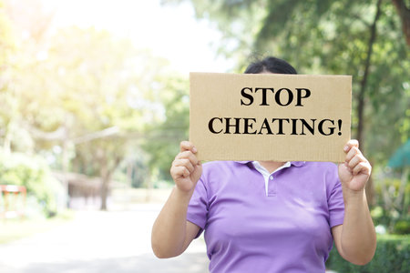 Woman protester holds paper placard with text Stop Cheating, outdoor background. Concept, campaign...