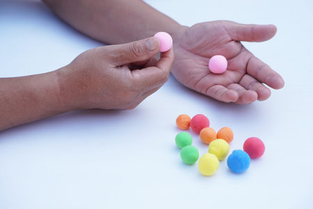 Close-up of hand holding a colored ball on white background.