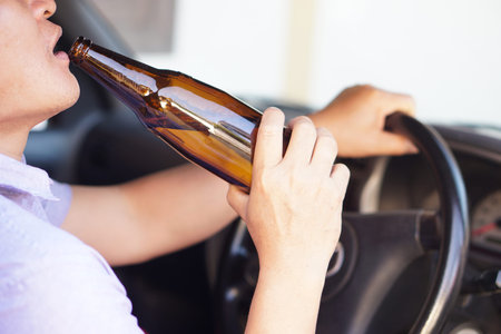 Man drinking beer while driving a car. Focus on the bottle.